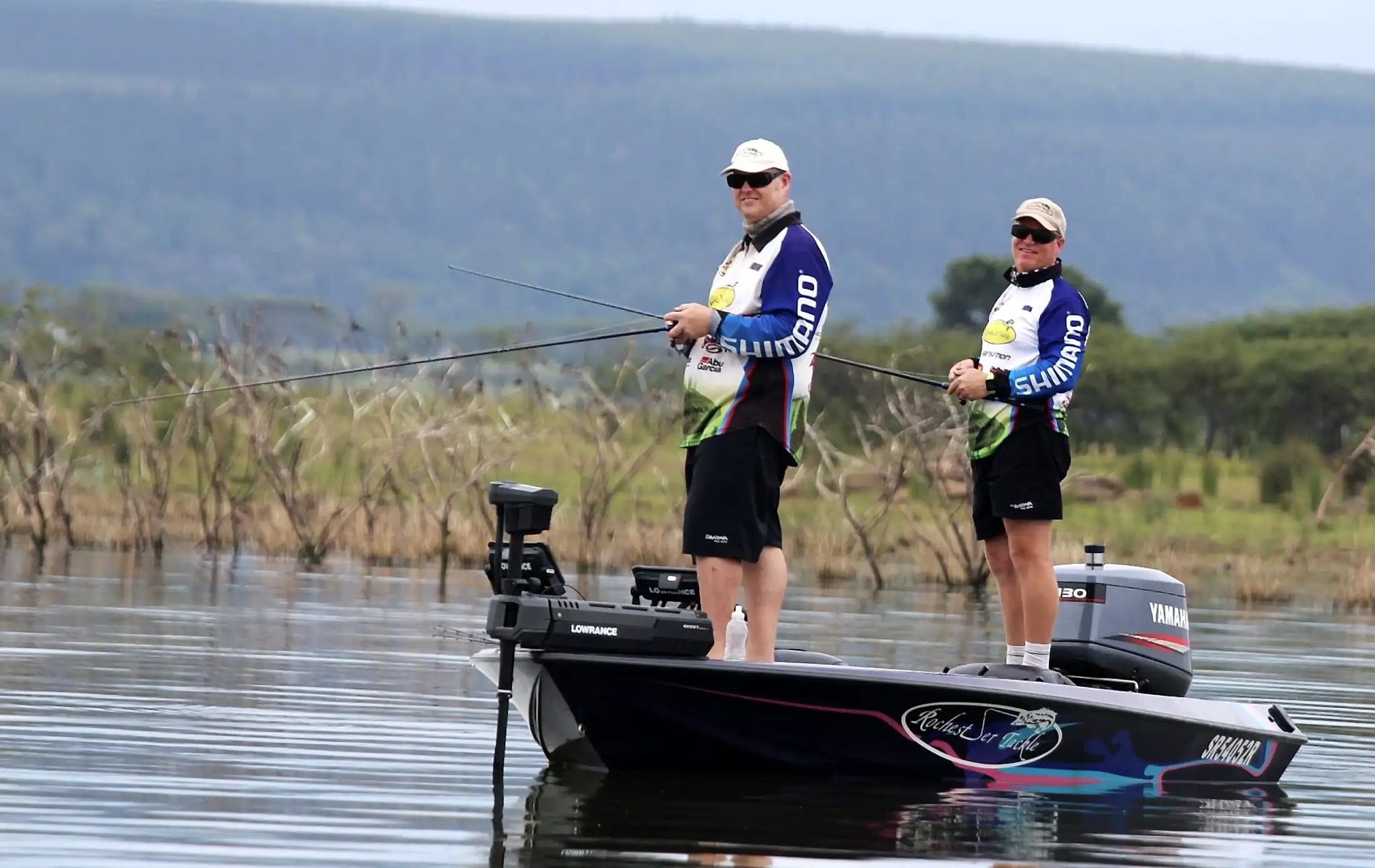 Two anglers casting from the Rochester boat past drowned trees at Albert Falls