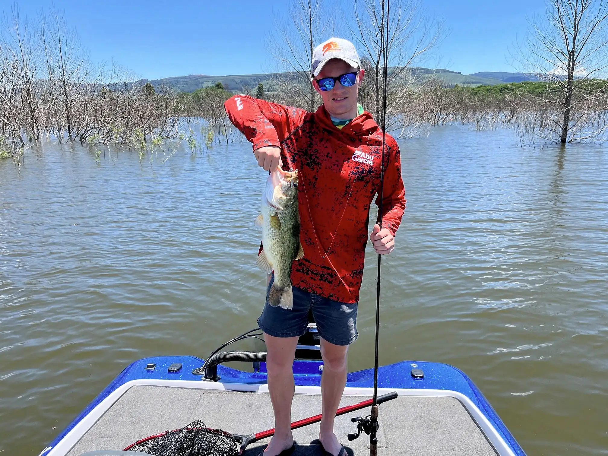 An angler in a red shirt holding a bass on a boat among flooded trees