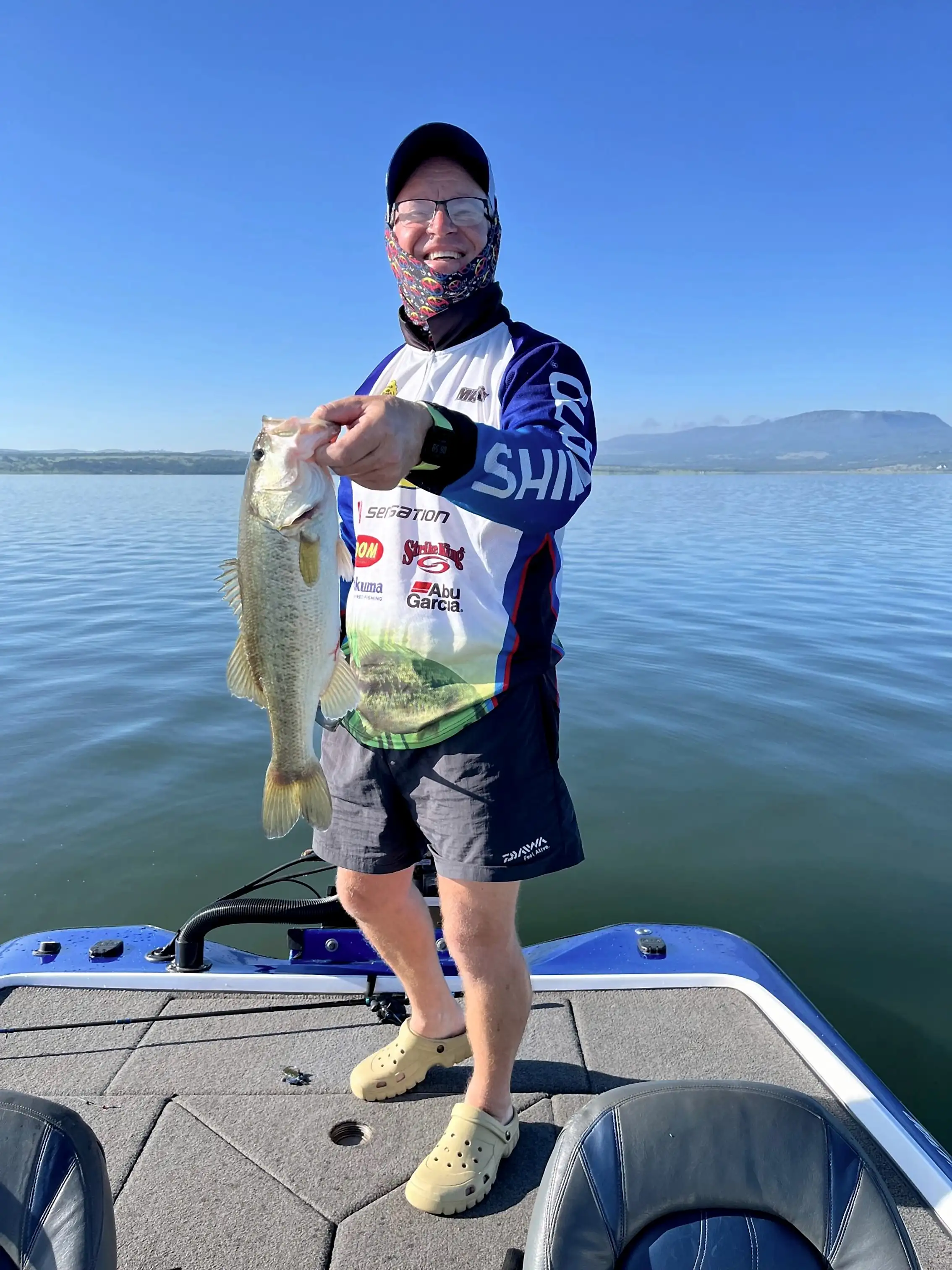 An angler in a Shimano tournament shirt holding up a largemouth bass on a boat deck
