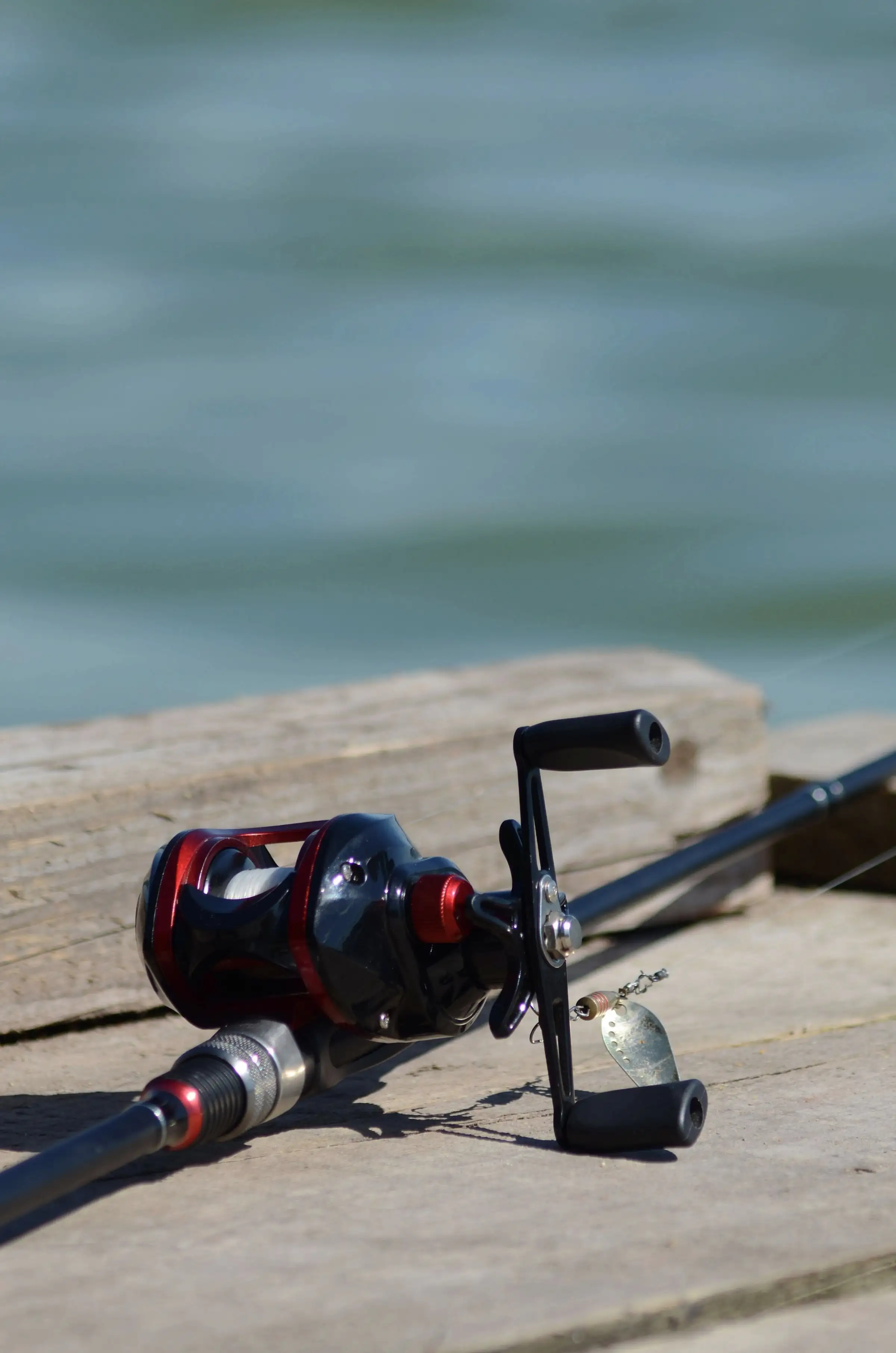A red baitcasting reel on a rod resting on a wooden jetty