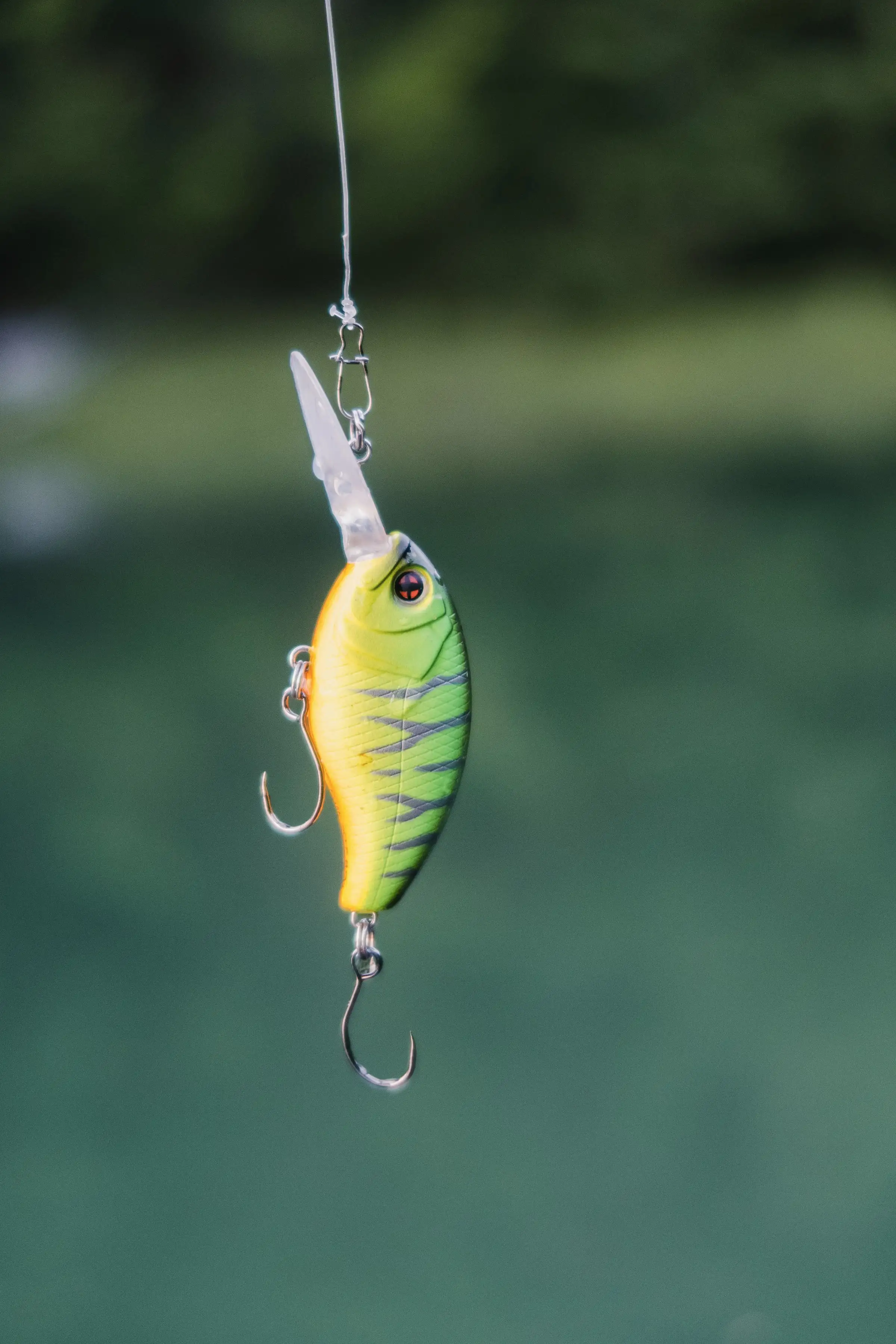 A yellow and green crankbait hanging from a rod over dark water