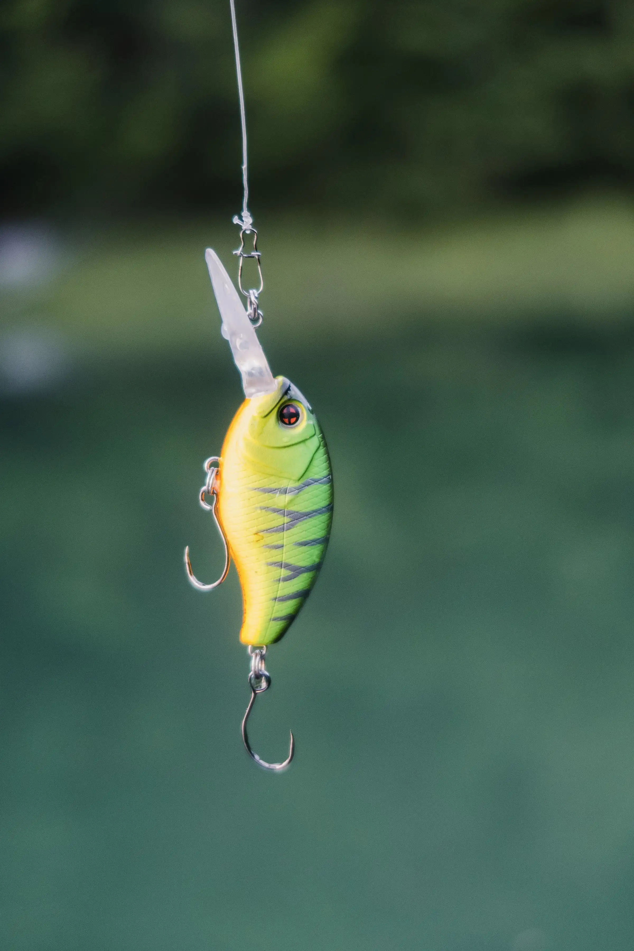 A yellow and green crankbait hanging from a rod over dark water