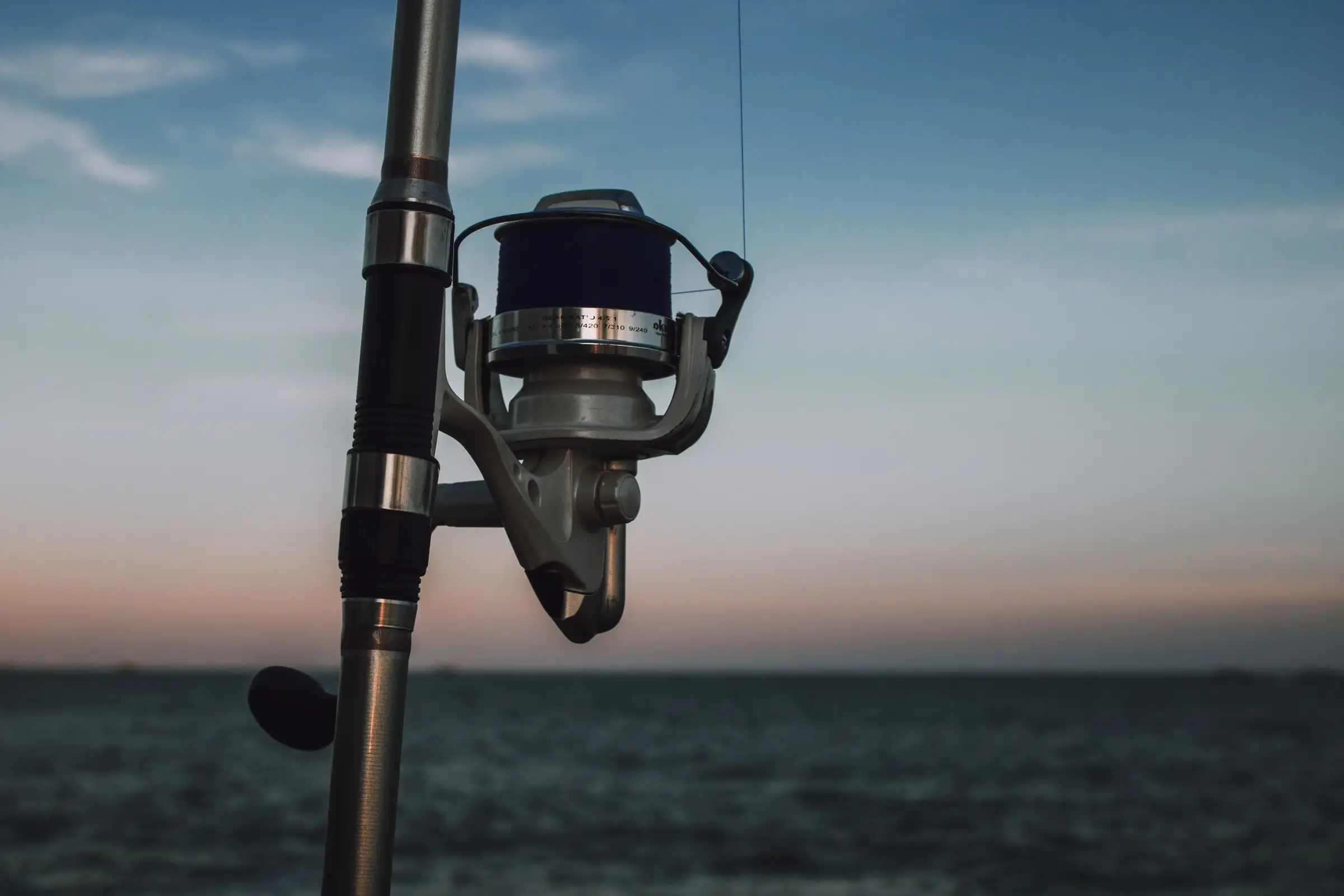A spinning reel on a rod held up against the sea at sunset