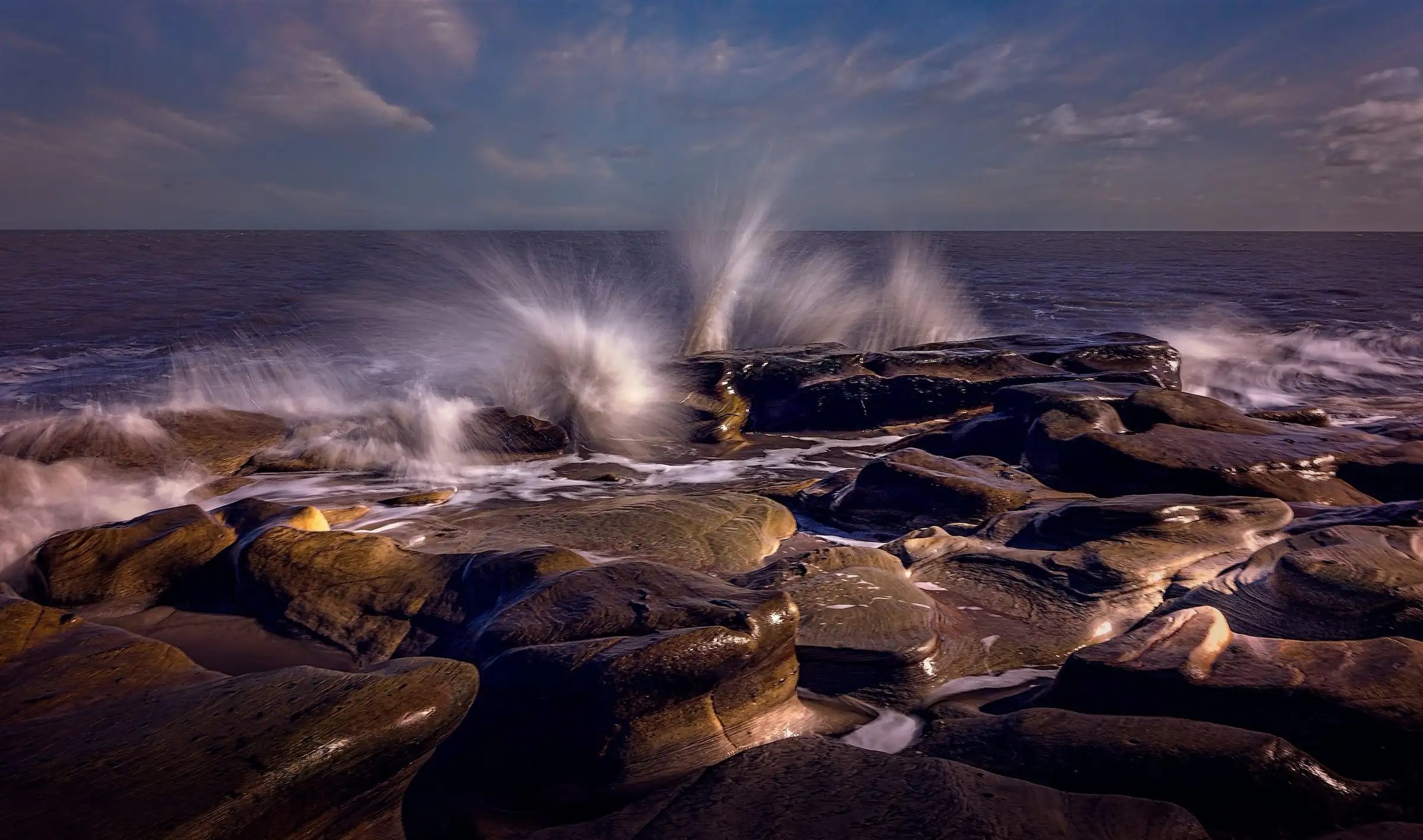 A wave breaking over coastal rocks at dusk
