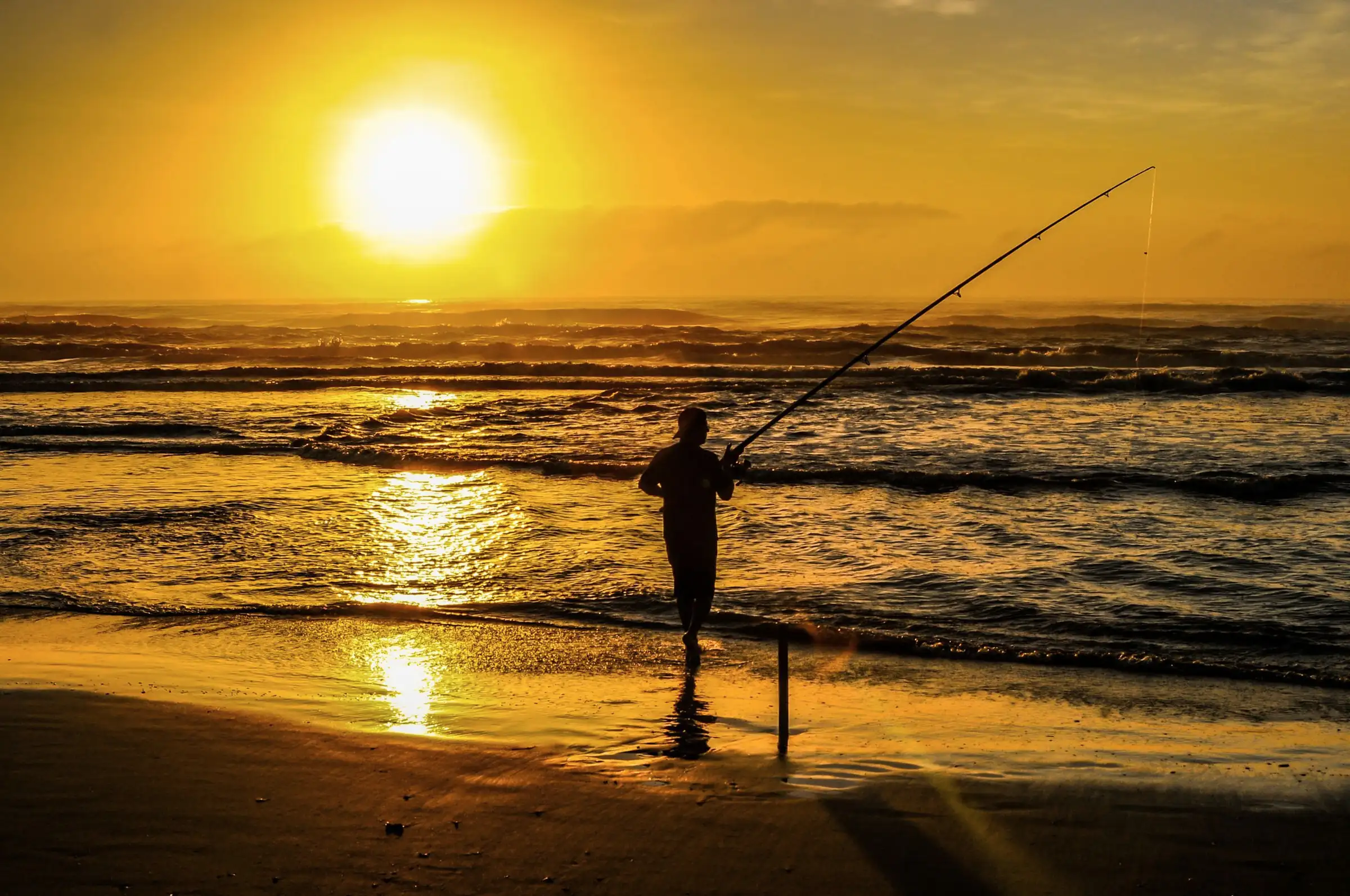 An angler casting into the surf at sunrise