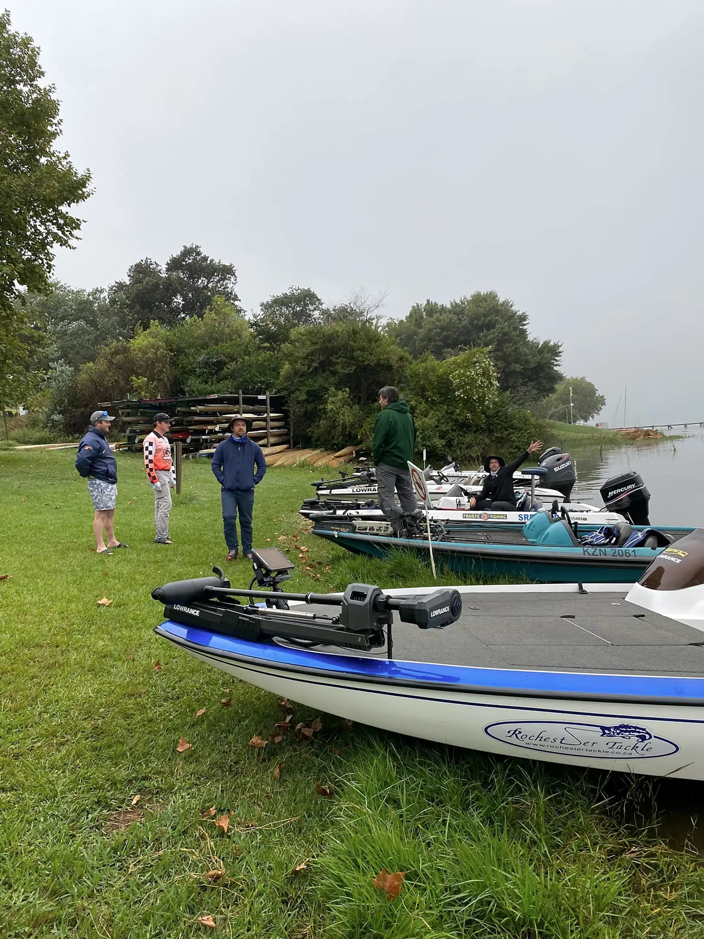Bass boats pulled up on a grassy bank with anglers getting ready in the mist